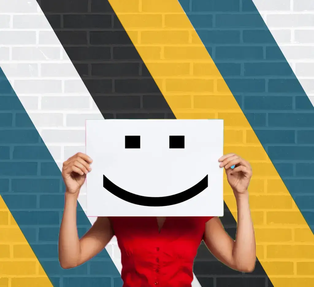 A woman holds up a smiley face paper against a brick wall. Affordable social media management