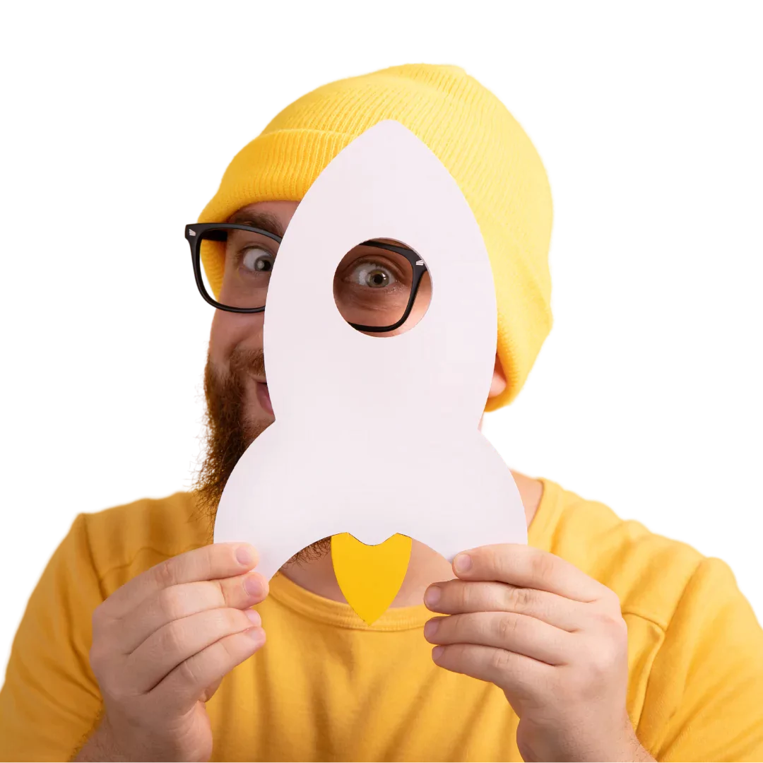 Man in yellow hat and glasses holds up paper rocket.